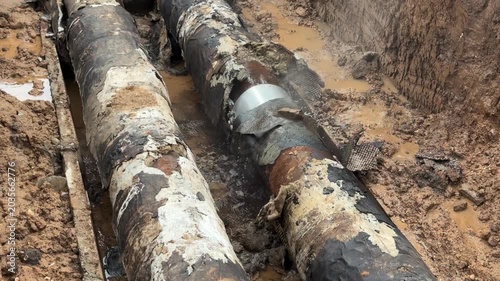 Steam and water jet escaping from corroded heating pipe with damaged insulation in excavation trench