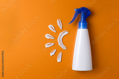 Bottle of sunscreen and texture of cream on colored background top view