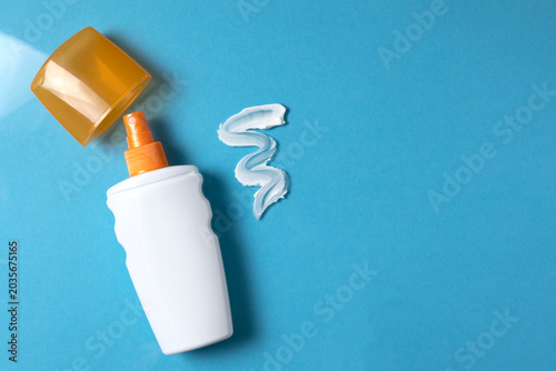 Bottle of sunscreen and texture of cream on colored background top view