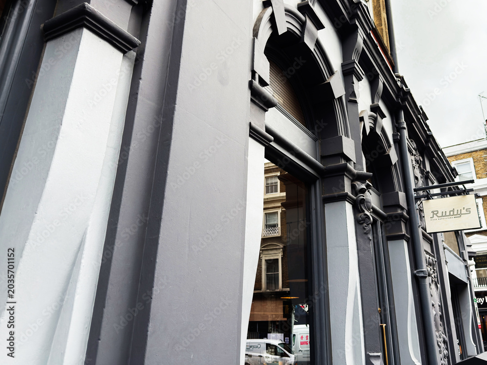 Fototapeta premium Historic gray Rudy's Pizza Napoletana architecture with ornate facade and street reflection in London, UK