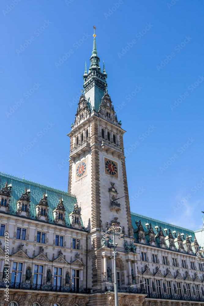 Fototapeta premium The majestic tower of Hamburg Town Hall rises against a vibrant blue sky, showcasing its neo-Renaissance architecture in Germany's historic city center.
