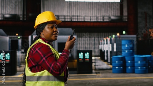 Fotografía Woman engineer, portable walkie-talkie, speak with colleagues, walking across warehouse, worker supervising machinery hall workstations, Wireless radio transceiver near sparks from welding