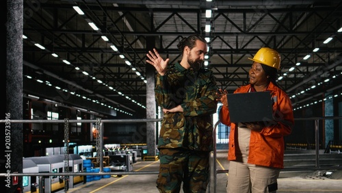 Photos Engineering specialist and armed forces officer inspect heavy machinery in large-scale facility, Wartime economy ensures military support and industrialization powering national defense mission