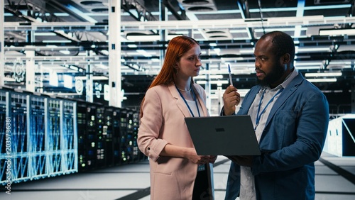 Картината върху платно Server farm manager teaching intern to use laptop and optimize electronics during induction, Data center team leader and trainee using notebook to monitor system performance, camera A