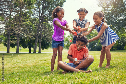 Happy, children and water balloons in park with fun, game and bonding together for childhood memories. Kids, smile and play outdoor with splash bomb, connection and entertainment for summer holiday.