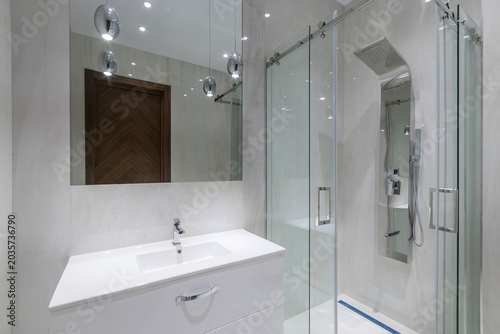 Elegant bathroom interior. Glass shower cabin with modern touch shower. Stylish lamps.
