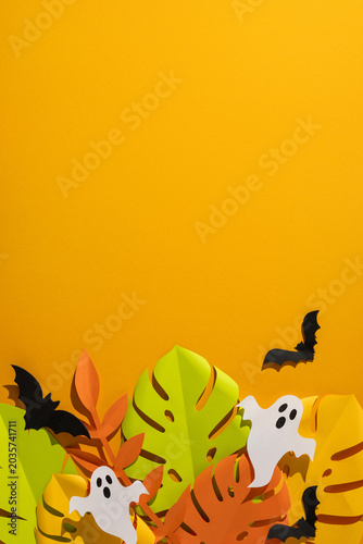 Tropical vertical Halloween paper leaves and ghost decorations with bats on bright orange background