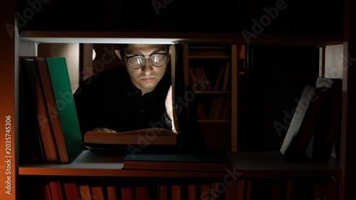 Photos Student reading an open book by flashlight in a dim library, focused on learning