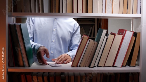 Photos Person inserting or retrieving a banknote between old books on a library shelf,