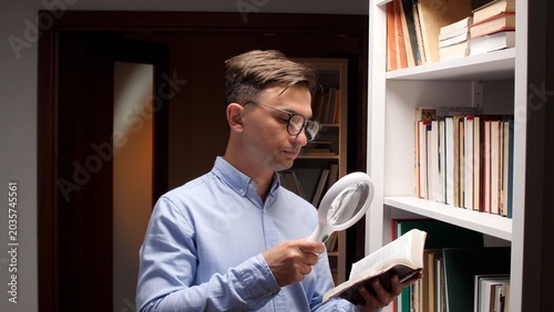 Foto Man wearing glasses closely examining a text in a book using a magnifying glass,