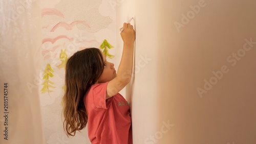 Fotografi Young girl focused on painting a colorful landscape mural directly on a textured