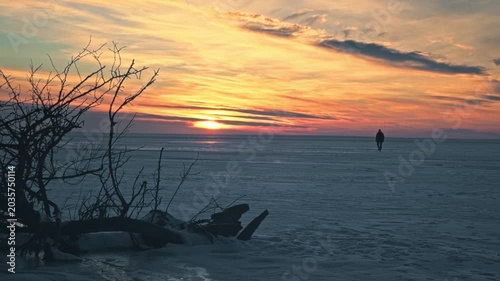 Lonely man walking thick ice frozen Dnieper River. Spectacular colorful winter sunset, dramatic golden hour light reflection snow covered surface. Cinematic peaceful majestic winter landscape Ukraine.
