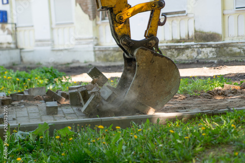 Tableau sur toile in the middle of the park area, the Excavator dismantles tiles on the sidewalk, breaking them with a bucket and raking them into a pile
