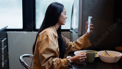 Foto Young woman enjoying breakfast while video calling, connecting virtually