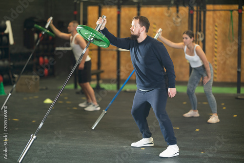 Foto Focused young bearded man in comfortable sportswear performing single arm landmi