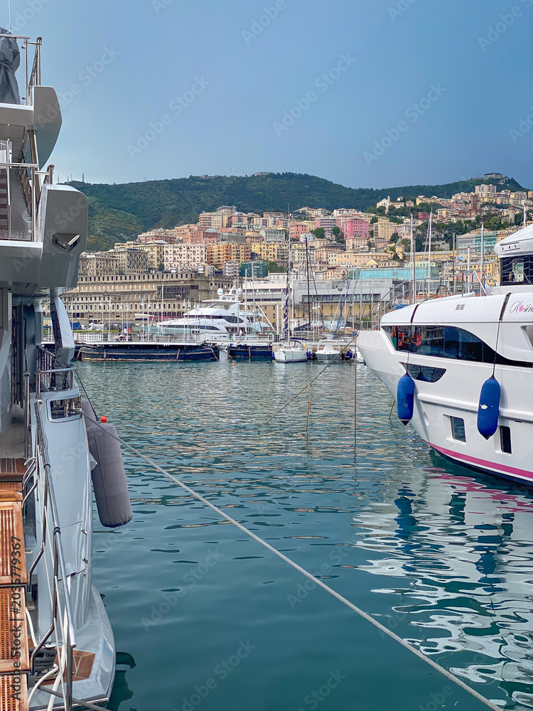 Obraz premium Yachts and sailboats moored in Porto Antico marina with a cruise ship and Genoa skyline against blue sky, Italy