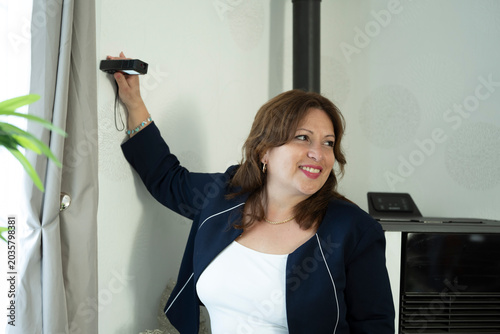 Smiling woman holding a laser distance meter while measuring an interior room, illustrating home renovation, real estate or interior planning.