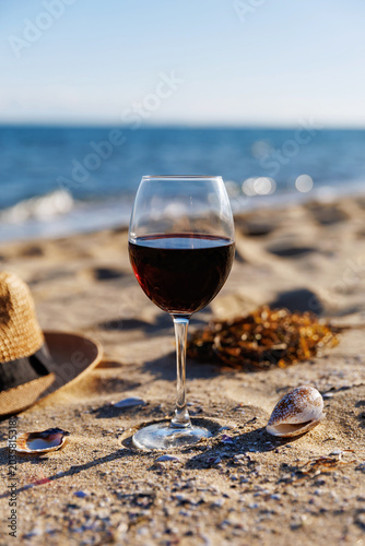 Minimal composition of red wine glass on sand with seashells and ocean background clean aesthetic summer lifestyle and coastal relaxation concept