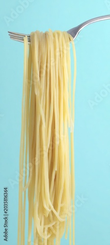 Vertical Spaghetti Noodles on Silver Fork with Light Blue Solid Background