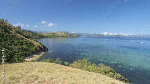 Panorama along the northern headland near Labuan Bajo in Komodo National Park, Indonesia, surrounded by vibrant coral reefs and turquoise tropical waters under a sunny blue sky