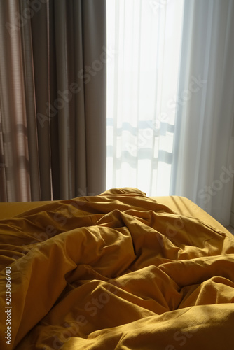 Slika na platnu An unmade bed with rumpled mustard yellow sheets is illuminated by soft morning