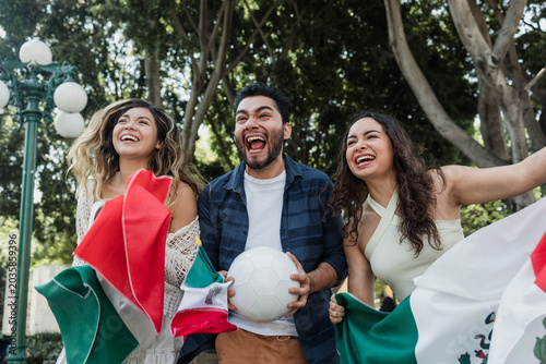 group of mexican soccer fans holding a soccer ball and national flag supporting to their sport team outdoors in Mexico city in Latin America
