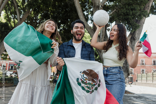 group of mexican soccer fans holding a soccer ball and national flag supporting to their sport team outdoors in Mexico city in Latin America