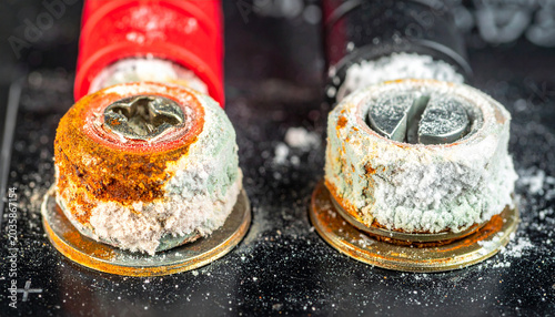 Corroded Battery Terminals: Close-up view of two heavily corroded and oxidized battery terminals, one showing reddish rust and the other white powder, indicating a need for maintenance.