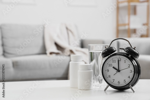 Canvas Print Alarm clock with pill bottles and glass of water on table in room