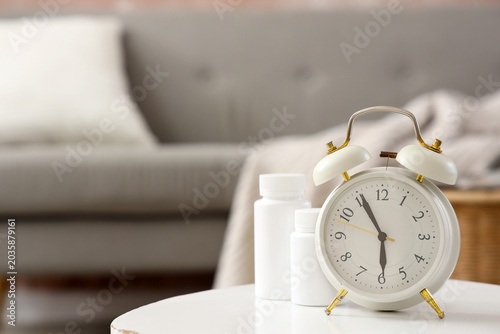 Foto Alarm clock with pill bottles on table in room, closeup