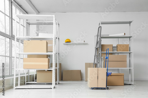 Foto Shelf units with cardboard boxes, trolley and stepladder in warehouse