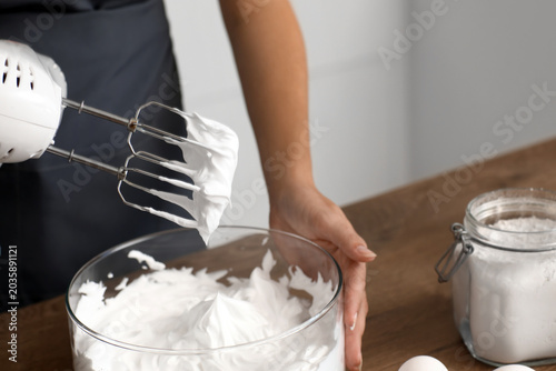 Photos Woman whipping egg albumen with mixer in kitchen, closeup