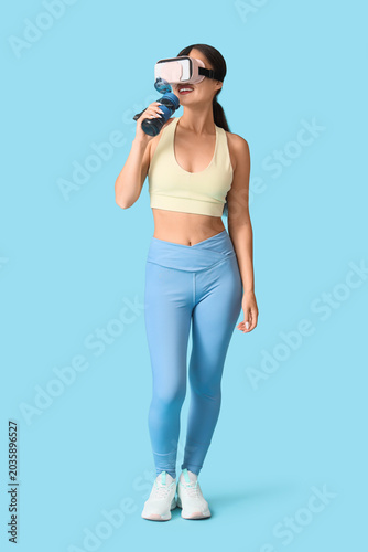 Sporty young woman in VR glasses with water bottle on blue background