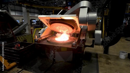 Cinematic industrial footage featuring molten metal pouring from a high-temperature furnace inside a modern manufacturing facility. Intense heat, glowing steel, sparks, heavy machinery, and industrial
