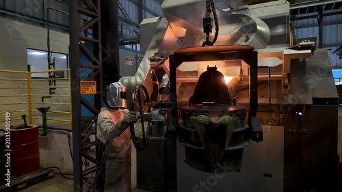Cinematic industrial footage featuring molten metal pouring from a high-temperature furnace inside a modern manufacturing facility. Intense heat, glowing steel, sparks, heavy machinery, and industrial