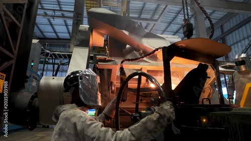 Cinematic industrial footage featuring molten metal pouring from a high-temperature furnace inside a modern manufacturing facility. Intense heat, glowing steel, sparks, heavy machinery, and industrial