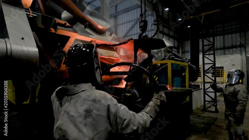 Cinematic industrial footage featuring molten metal pouring from a high-temperature furnace inside a modern manufacturing facility. Intense heat, glowing steel, sparks, heavy machinery, and industrial