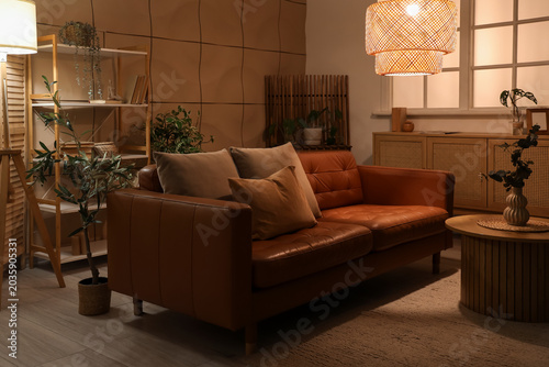 Foto Interior of dark living room with brown sofa, plants and glowing lamps at night