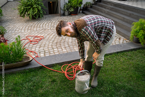 Konstfotografi Gardener filling watering can with the hose and looking at camera