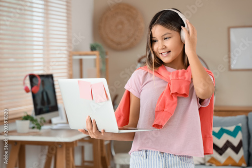 Happy teenage Asian girl in headphones with laptop on online lesson at home