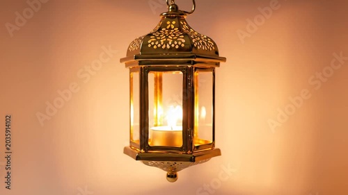 Decorative gold lantern with lit candle on warm background