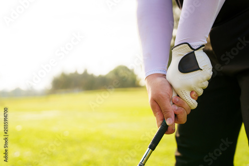 Golfer standing on green fairway, close up on hand holding golf club.