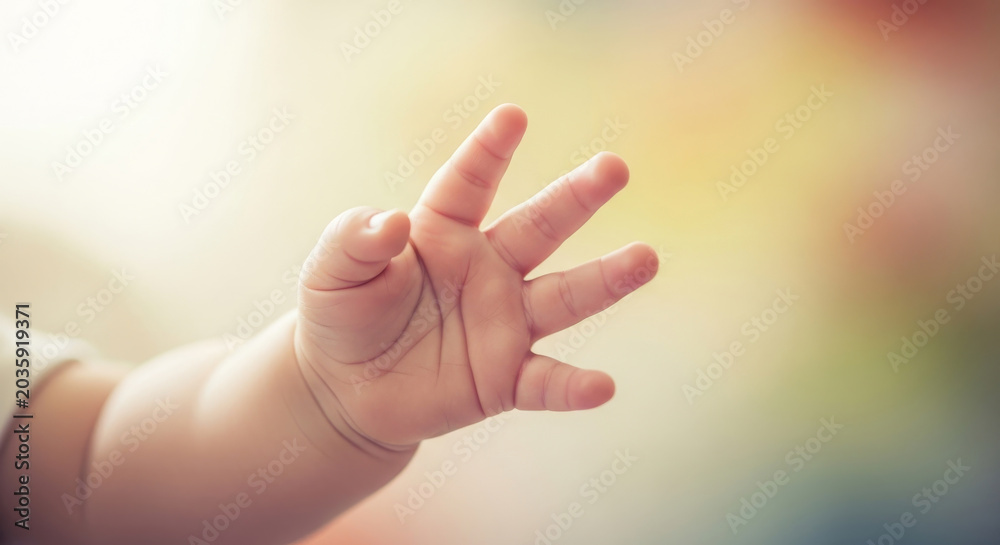 Obraz premium Close up of cute baby hand reaching out, tiny newborn fingers with soft pastel bokeh background, hope and new life concept