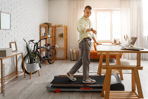 Young man looking at smartwatch on treadmill in office