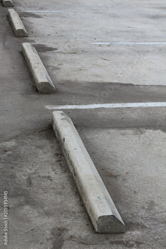 Concrete parking stops line a weathered asphalt lot with white painted markers