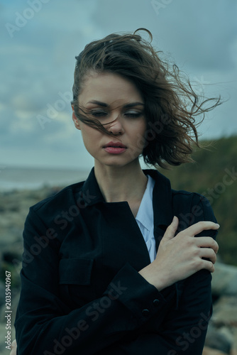 Bild auf Leinwand Moody outdoor image of a woman with windblown hair near the coast, wearing a dar