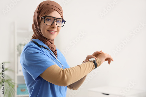 Female Muslim doctor looking at wristwatch in clinic