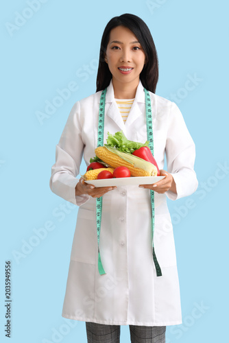 Female Asian nutritionist with vegetables on blue background