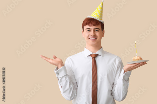 Young man with piece of birthday cake on beige background
