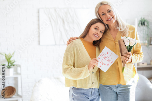 Young woman greeting her mother with tulips and card at home
